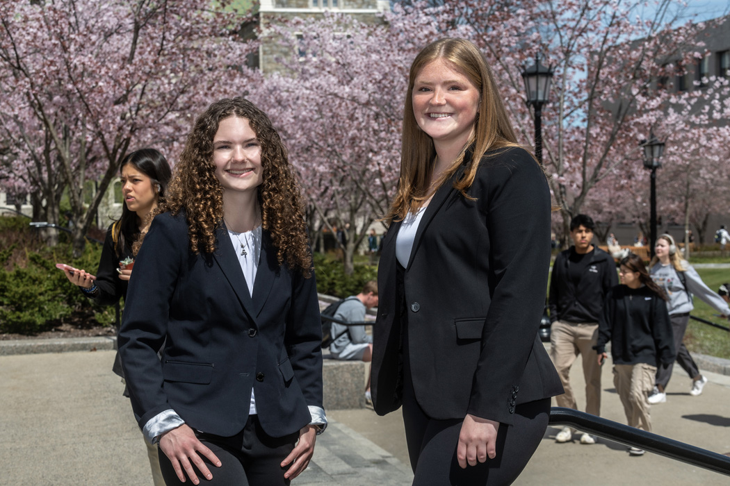 Meghan Heckelman and Katie Garrigan on campus in front of flowering cherry trees