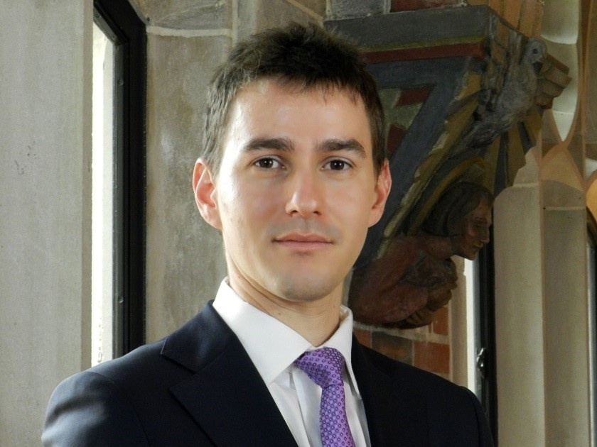 Photo of Headshot of young professor in dark coat and pastel tie