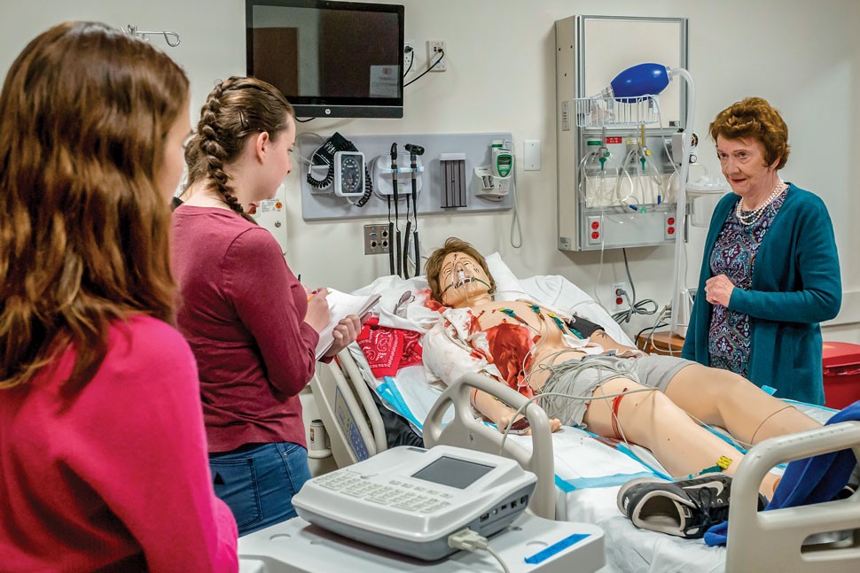 Professor Ann Burgess with students and a mannequin in a hospital bed.