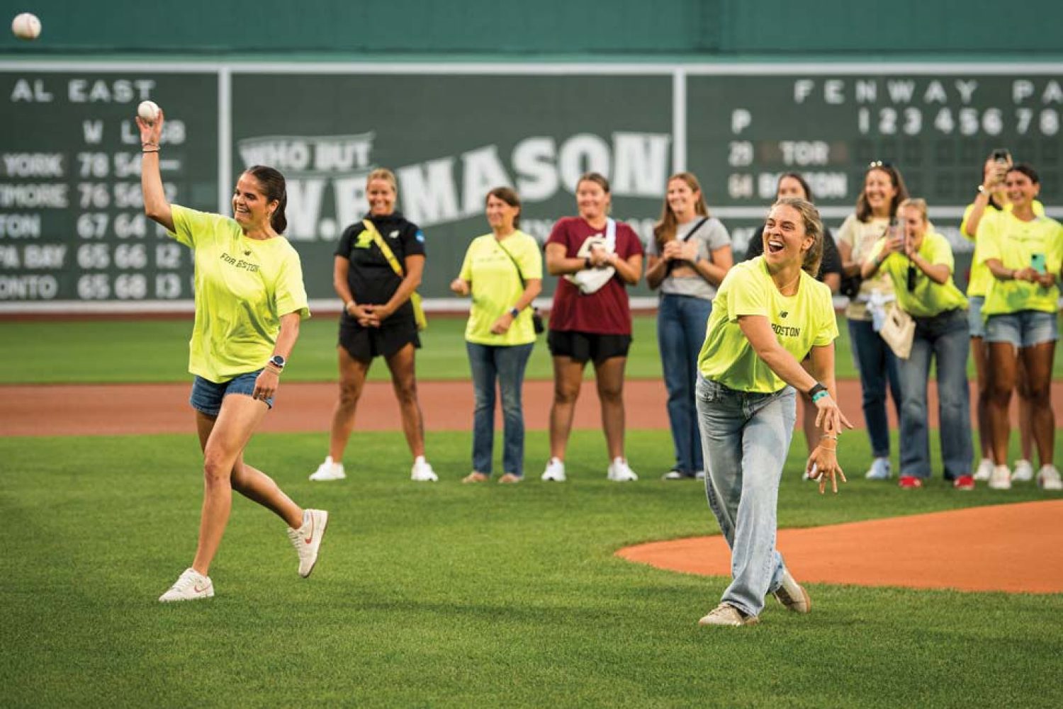 Two BC Lacrosse players throwing the first pitch with the team and coaching staff in the background