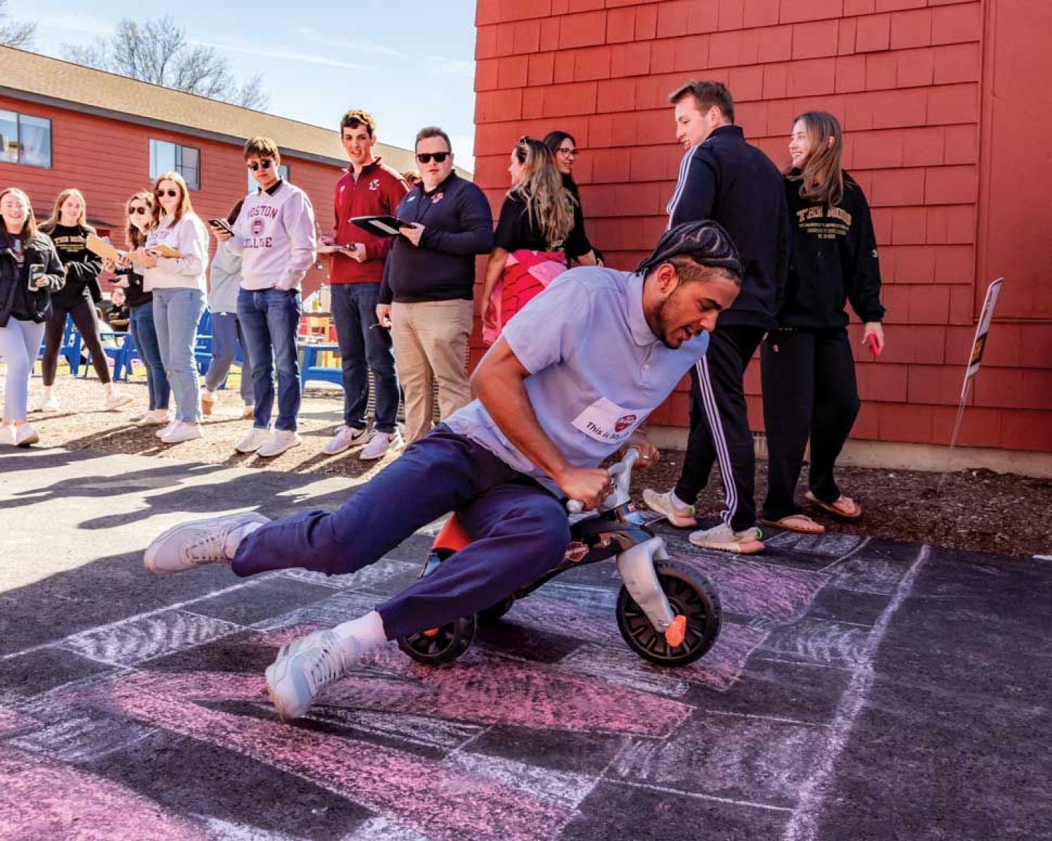 Miles Hester ’24 crosses a chalk drawn finish line on a trike with fellow student onlookers.