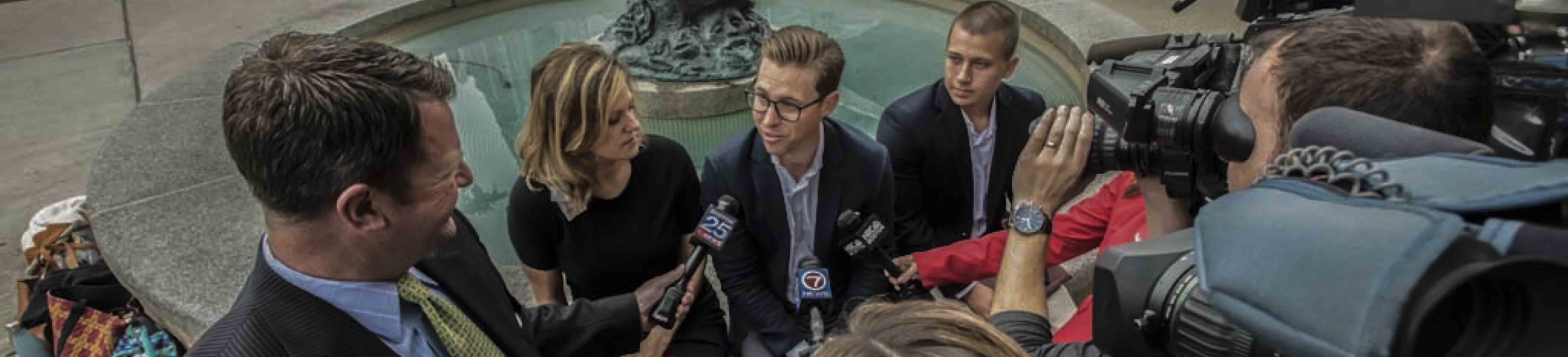 three people in business attire speak to reporters