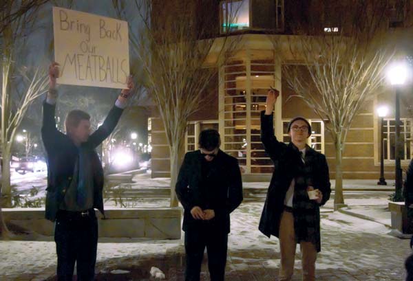 Three students, one holding a sign stating "Bring back the meatballs" outside Corcoran Commons