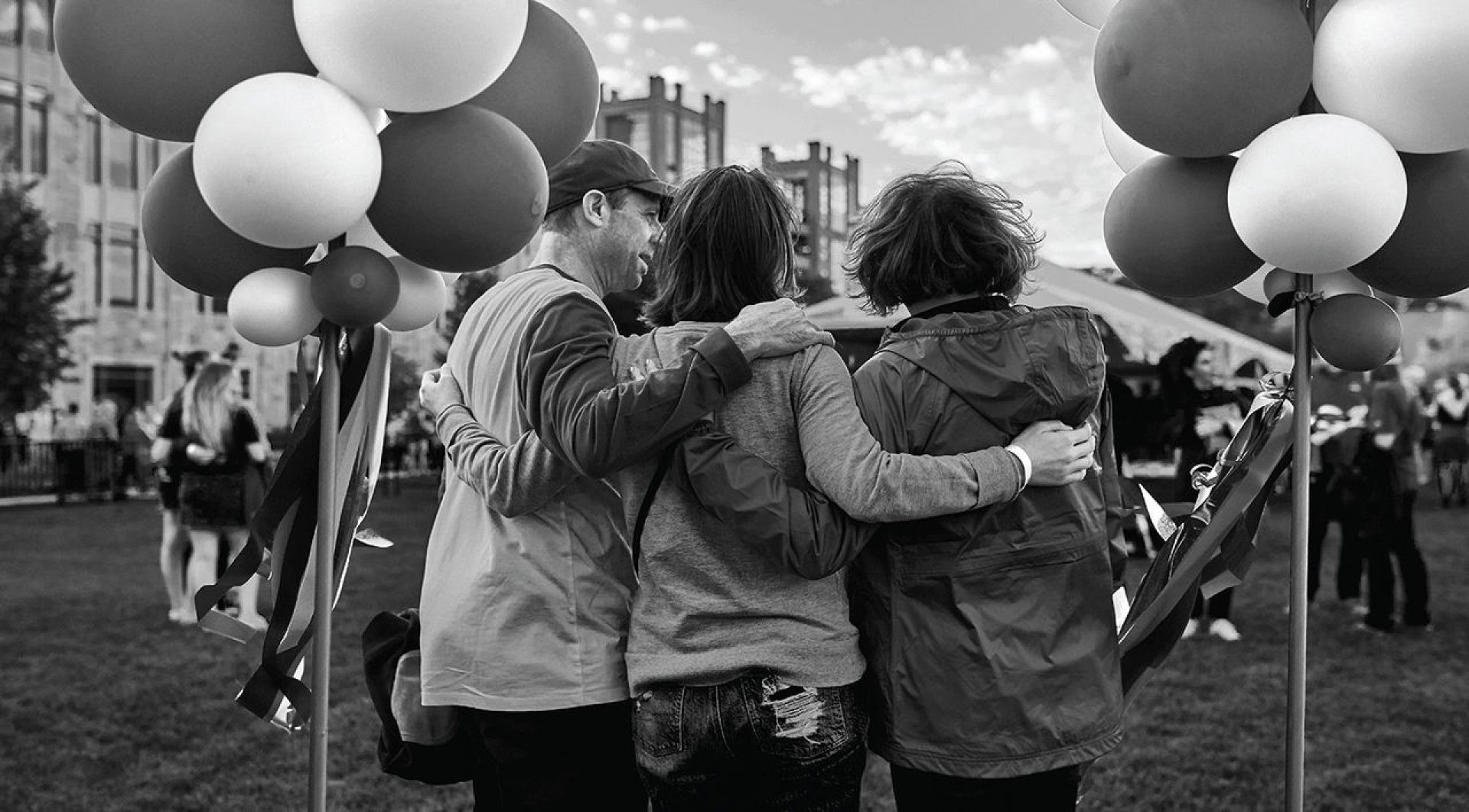 Black and white photo of the back of a family holding balloons on campus